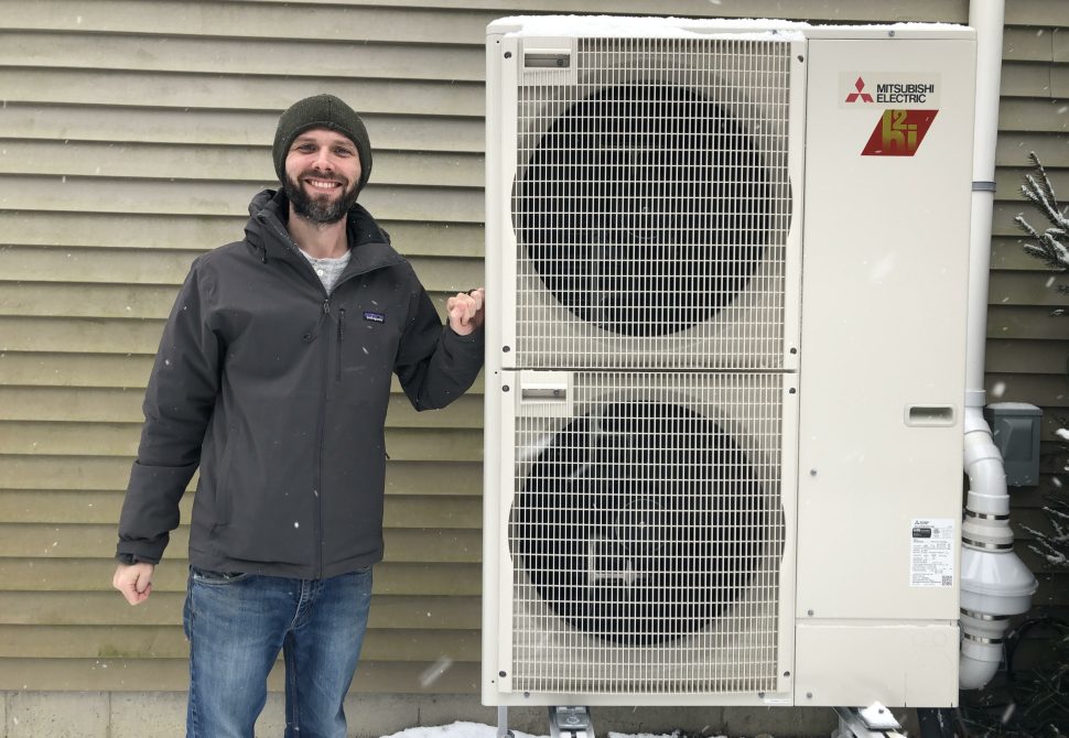Homeowner beside the cold-climate heat pump in falling snow